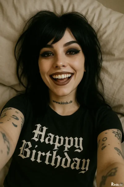 Dieses Spruch-Bild zeigt eine junge Frau mit dunklen Haaren, ausdrucksstarkem Make-up und Piercing, die auf einem Kissen liegt und die Kamera direkt anlächelt. Ihr schwarzes T-Shirt trägt den Schriftzug „Happy Birthday“ in gotischer Typografie. Auf dem Hals ist die Webadresse „www.kirds.de“ tätowiert, auf den Armen sind verschiedene Tattoos zu sehen. Das Bild strahlt Lebensfreude, Selbstbewusstsein und einen alternativen Stil aus.