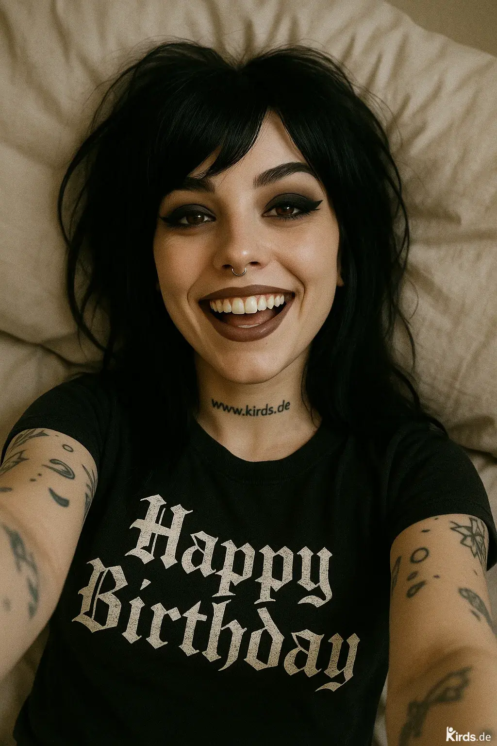 Dieses Spruch-Bild zeigt eine junge Frau mit dunklen Haaren, ausdrucksstarkem Make-up und Piercing, die auf einem Kissen liegt und die Kamera direkt anlächelt. Ihr schwarzes T-Shirt trägt den Schriftzug „Happy Birthday“ in gotischer Typografie. Auf dem Hals ist die Webadresse „www.kirds.de“ tätowiert, auf den Armen sind verschiedene Tattoos zu sehen. Das Bild strahlt Lebensfreude, Selbstbewusstsein und einen alternativen Stil aus.